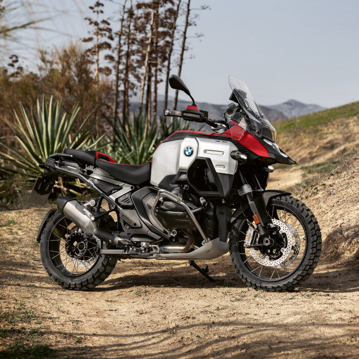 Ein BMW Adventure-Motorrad mit robusten Reifen und einer rot-silbernen Karosserie steht auf einem Feldweg im Freien, umgeben von trockenen Pflanzen und Hügeln - bereit für Ihre nächste Fahrt bei den BMW Probefahrtwochen Werdohl. Rider's Point der Kaltenbach Gruppe. Dein Partner für BMW Motorrad und Honda.