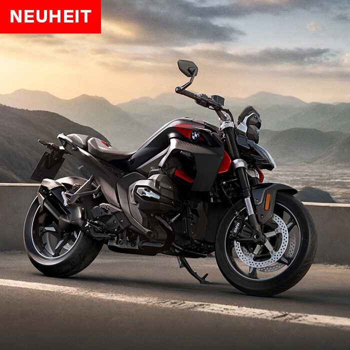 Ein schnittiges schwarz-rotes BMW-Motorrad ist auf einem Aussichtspunkt geparkt, mit Bergen und einem bewölkten Himmel im Hintergrund. Oben links ist ein rotes Schild mit der Aufschrift NEUHEIT - jetzt mit BMW Probefahrtwochen Werdohl zu sehen. Rider's Point der Kaltenbach Gruppe. Dein Partner für BMW Motorrad und Honda.