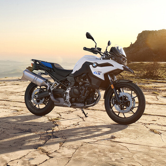 Ein weißes BMW Adventure Motorrad, geparkt auf einem felsigen Gelände bei Sonnenuntergang, mit fernen Bergen und einem klaren Himmel im Hintergrund - erleben Sie diesen Nervenkitzel bei den BMW Probefahrtwochen Werdohl. Rider's Point der Kaltenbach Gruppe. Dein Partner für BMW Motorrad und Honda.