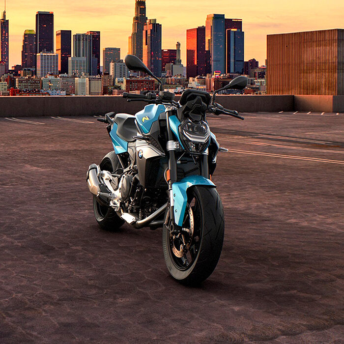 Ein blau-schwarzes Motorrad steht bei Sonnenuntergang auf einem leeren Dach mit der Skyline der Stadt im Hintergrund, bereit für die BMW Probefahrtwochen Werdohl. Rider's Point der Kaltenbach Gruppe. Dein Partner für BMW Motorrad und Honda.