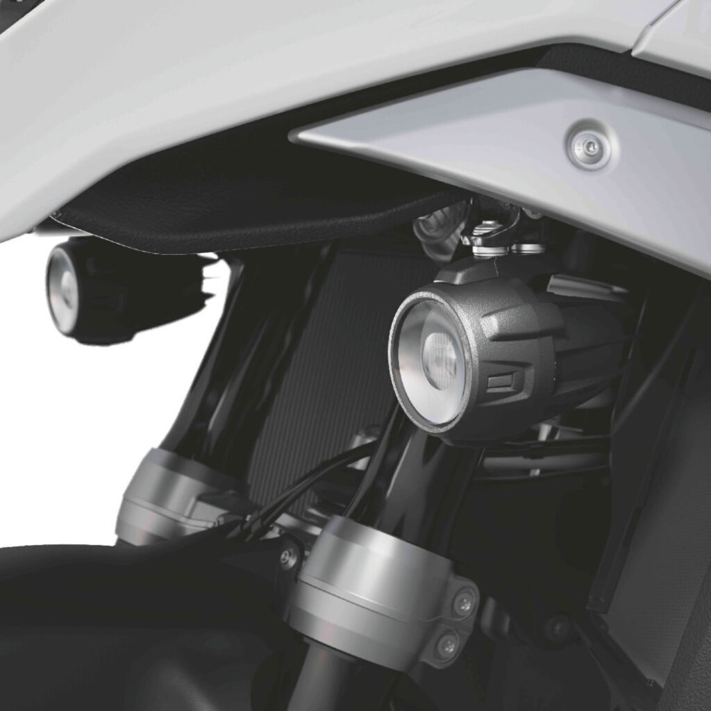 Nahaufnahme der Vorderradaufhängung und des Gabelbereichs eines Motorrads mit zwei LED-Zusatzscheinwerfern, die sicher in der Nähe des Rads unter dem weißen Kotflügel angebracht sind. Rider's Point der Kaltenbach Gruppe. Dein Partner für BMW Motorrad und Honda.