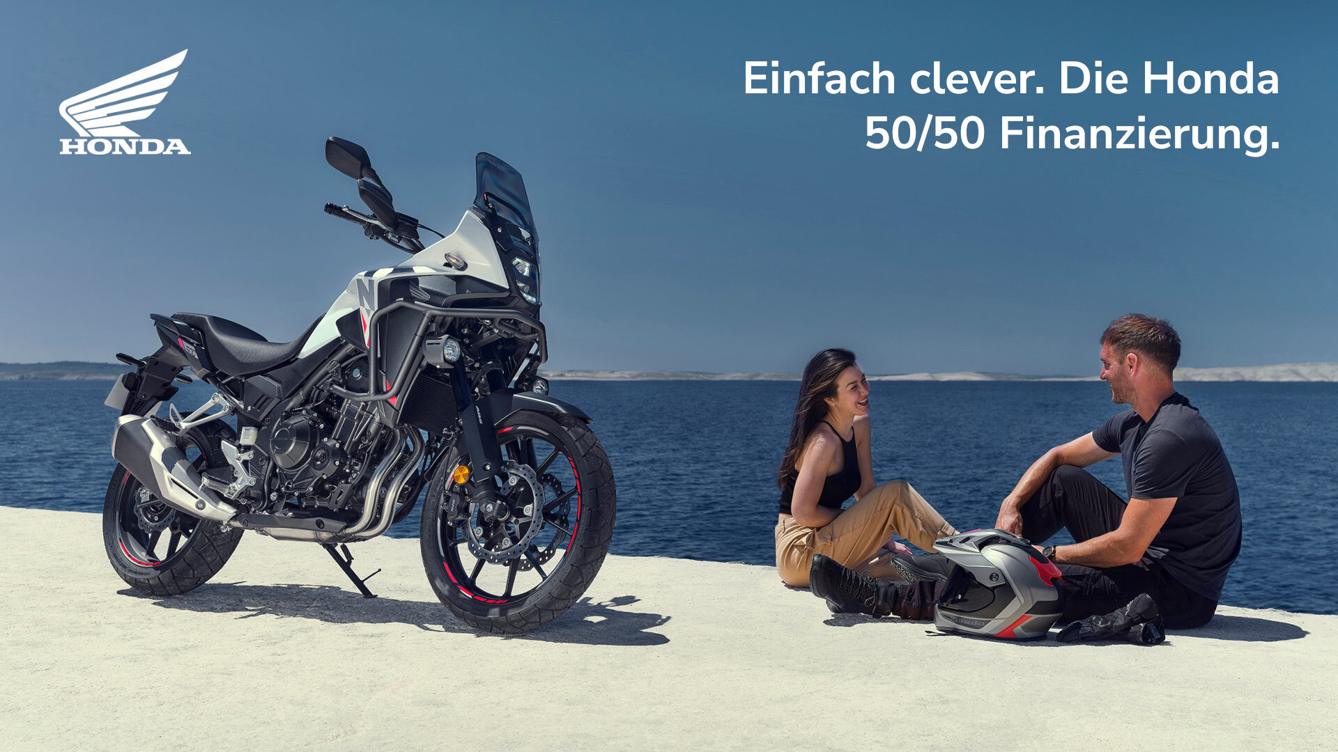 Ein Mann und eine Frau sitzen am Meer neben einem silbernen Honda-Motorrad. Der Mann hält einen Helm, während sie sich gegenseitig anlächeln. Der deutsche Text lautet: Einfach clever. Die Honda Finanzierung 50/50. Das Honda-Logo befindet sich oben links. Rider's Point der Kaltenbach Gruppe. Dein Partner für BMW Motorrad und Honda.