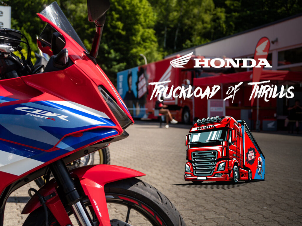 Nahaufnahme eines roten und blauen Honda CBR-Motorrads mit einem Truckload of Thrills-Honda-Veranstaltungsbanner und einem illustrierten roten Honda-Truck im Hintergrund, im Freien in der Nähe des Honda-Probefahrttrucks und -Anhängers. Rider's Point der Kaltenbach Gruppe. Dein Partner für BMW Motorrad und Honda.