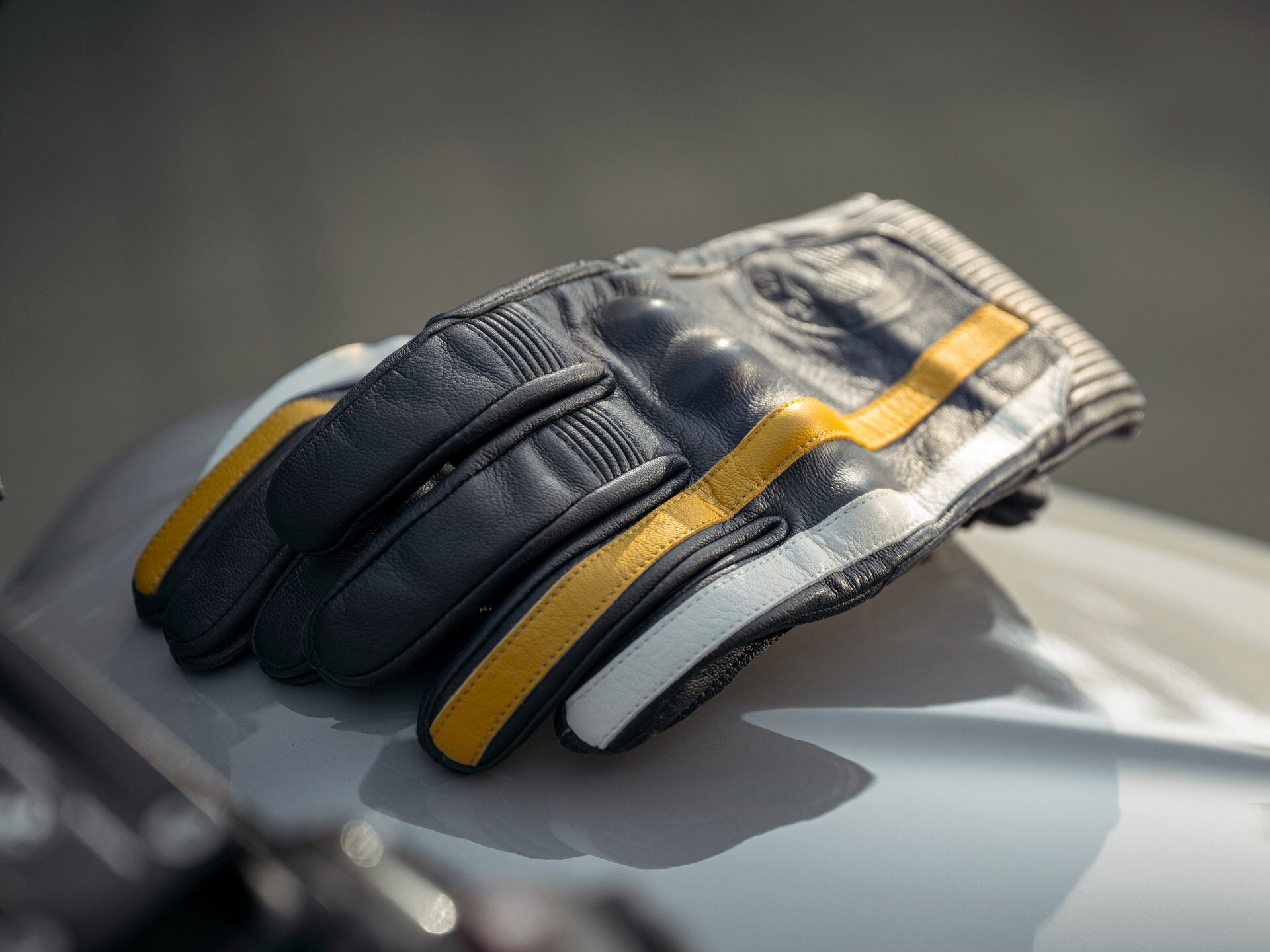 Ein Paar schwarzer Wunderlich-Lederhandschuhe mit gelben und weißen Streifen ruht auf einer glatten, hellen Oberfläche in sanfter Beleuchtung. Rider's Point der Kaltenbach Gruppe. Dein Partner für BMW Motorrad und Honda.