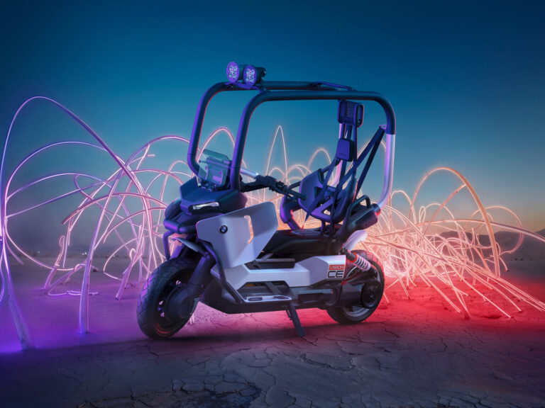 Ein futuristischer BMW Vision CE Elektroroller mit Überrollkäfig und Off-Road-Scheinwerfern steht auf rissigem Wüstenboden, umgeben von wirbelnden neonpinken und orangefarbenen Lichtspuren vor einem düsteren blauen Himmel. Rider's Point der Kaltenbach Gruppe. Dein Partner für BMW Motorrad und Honda.