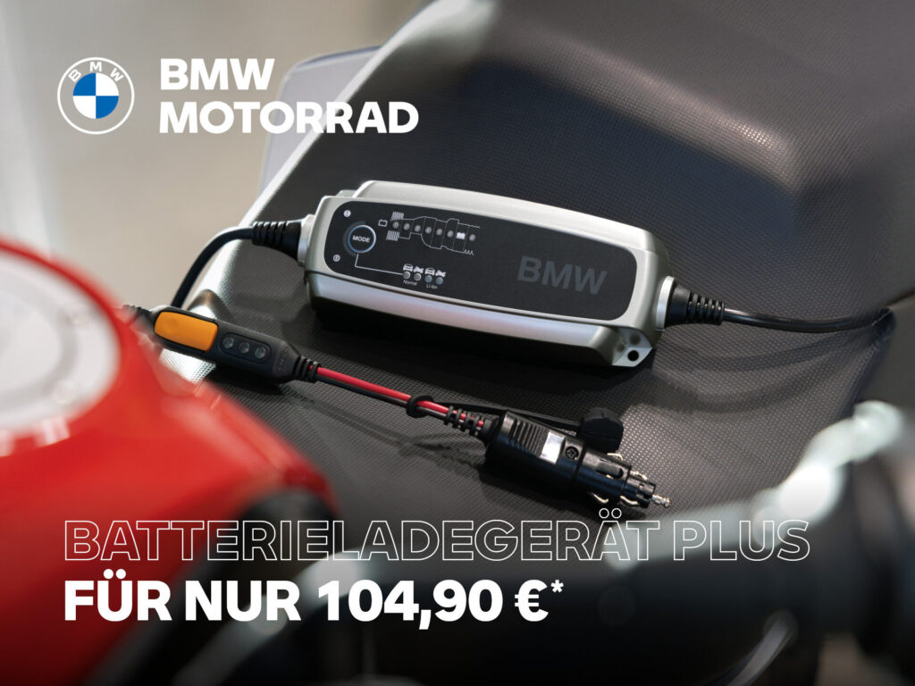 Ein BMW Batterieladegerät Plus ruht auf einem dunklen Motorradsitz, verbunden mit Kabeln. Ein Text in deutscher Sprache bewirbt das Ladegerät für 104,90 €. Das BMW Motorrad Logo befindet sich in der oberen linken Ecke. Rider's Point der Kaltenbach Gruppe. Dein Partner für BMW Motorrad und Honda.