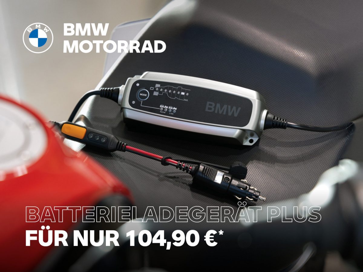 Ein BMW Batterieladegerät Plus ruht auf einem dunklen Motorradsitz, verbunden mit Kabeln. Ein Text in deutscher Sprache bewirbt das Ladegerät für 104,90 €. Das BMW Motorrad Logo befindet sich in der oberen linken Ecke. Rider's Point der Kaltenbach Gruppe. Dein Partner für BMW Motorrad und Honda.